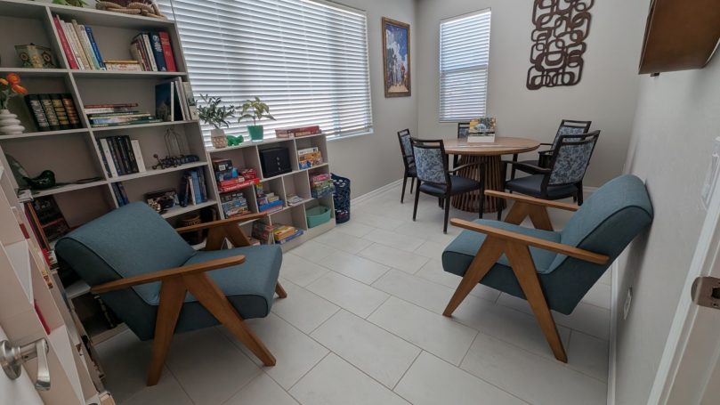 Library and activity room at Desert Willow Memory Care with books, games, and comfortable seating.